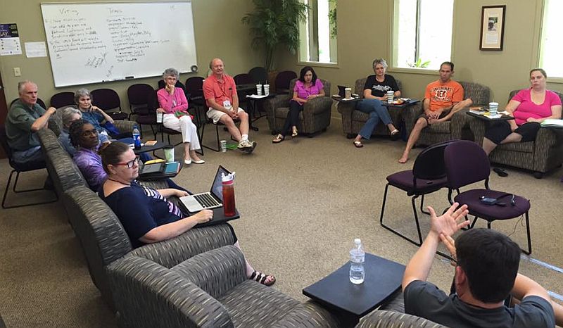 group sitting in chairs in a room, discussing business, a wallboard has many notes