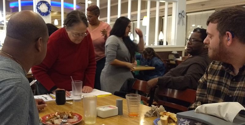 a group of people sit around a restaurant table, signing.