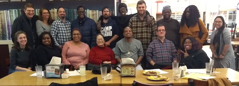 a group of seventeen people gather for a picture at a table.