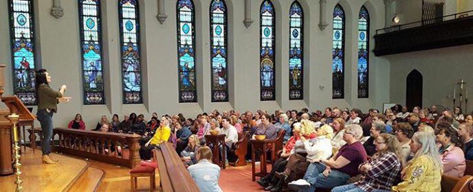 a side view, traditional church interior, full of people at the concert, with Megg Rose on the platform at the left.