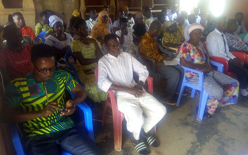 photo inside a meeting house, people seating and most are listening to a speaker.