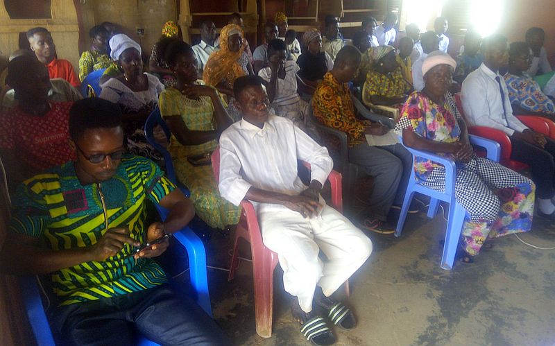 photo inside a meeting house, people seating and most are listening to a speaker.